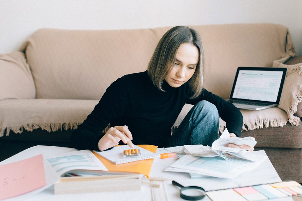 A young girl types on a calculator and looks through a pile of receipts.